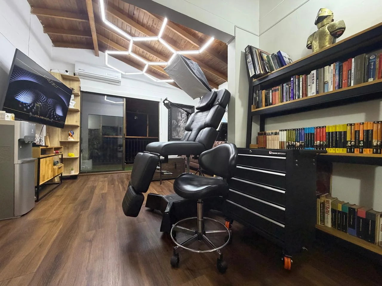 Estudio privado de Daniel Muñoz en Laureles, con camilla de tatuaje, iluminación hexagonal y biblioteca